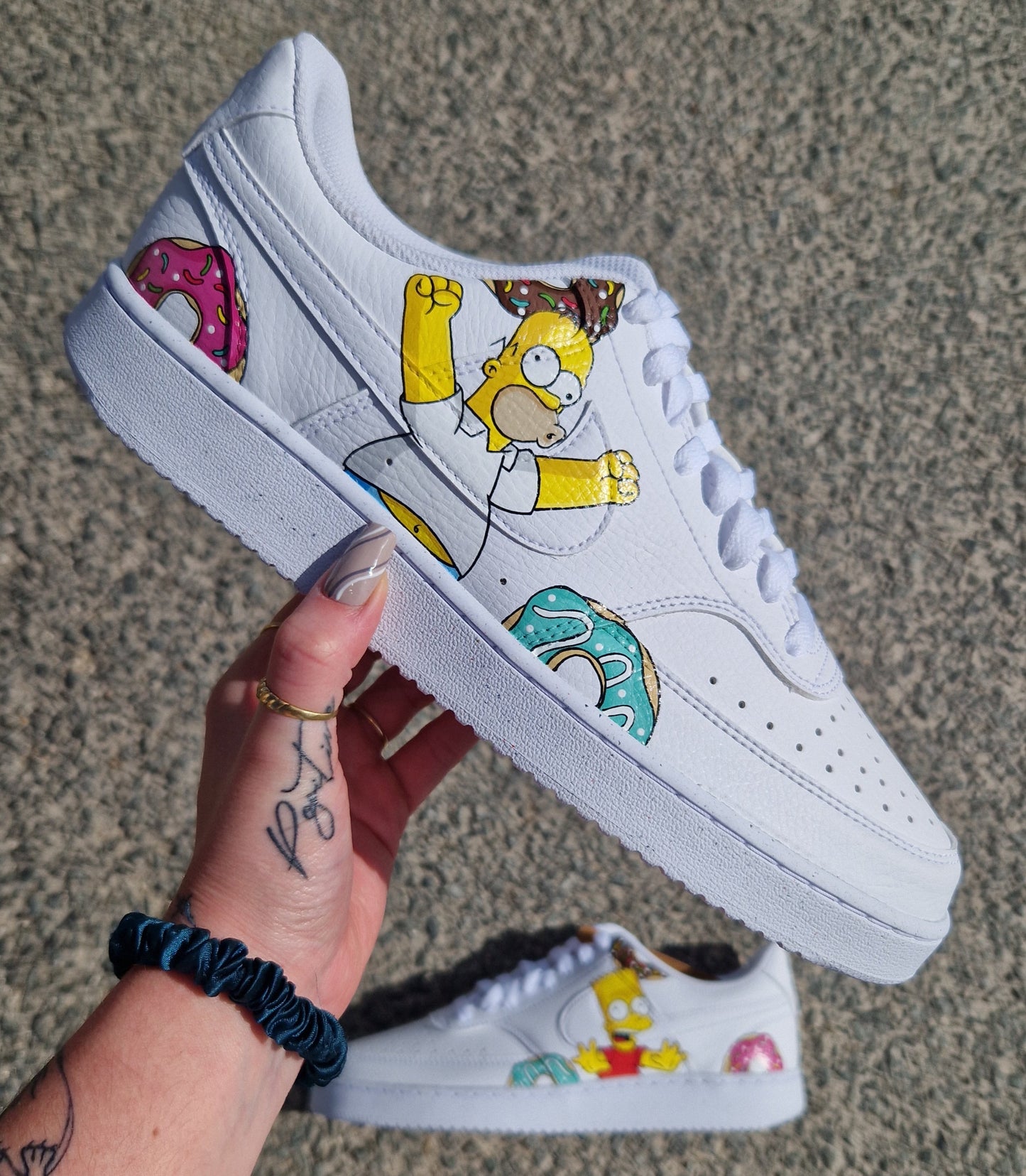 Photo d’une paire de Nike Court Vision Low personnalisée à la main, avec Bart sur une chaussure entouré de donuts, et Homer sur l’autre entouré de trois donuts. Peinture professionnelle résistante à l’eau. Disponible aussi sur Nike Air Force 1.