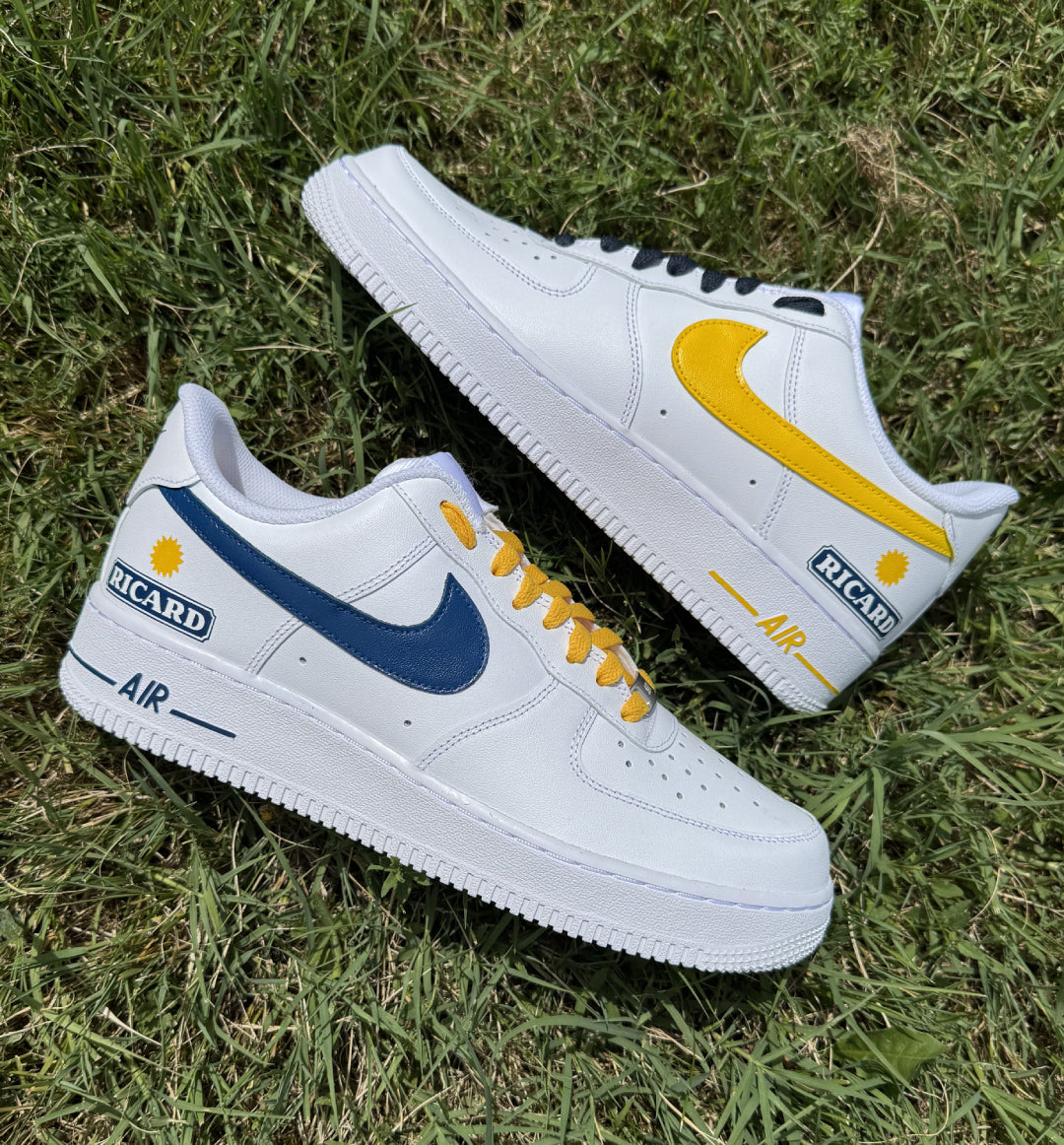 Par de Nike Air Force 1 personalizadas a mano con diseño Ricard, swooshes en azul y amarillo y logo Ricard en la parte trasera.