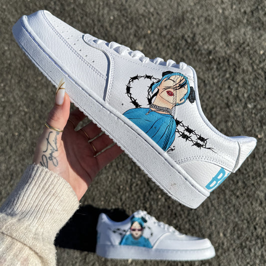 Nike personalizadas de Billie Eilish en azul con retratos pintados a mano, alambres de púas negros alrededor de los swoosh e inscripciones "Billie" y "Eilish" en la parte trasera. Modelo visible: Nike Court Vision Low.