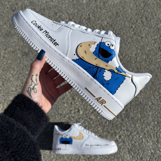 Nike Air Force 1 custom Cookie Monster peinte à la main, avec le monstre bleu tenant et croquant le swoosh Nike