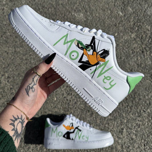 Nike Air Force 1 custom avec Daffy Duck peint à la main sur chaque chaussure et le mot "Money" en gros sur les côtés externes.