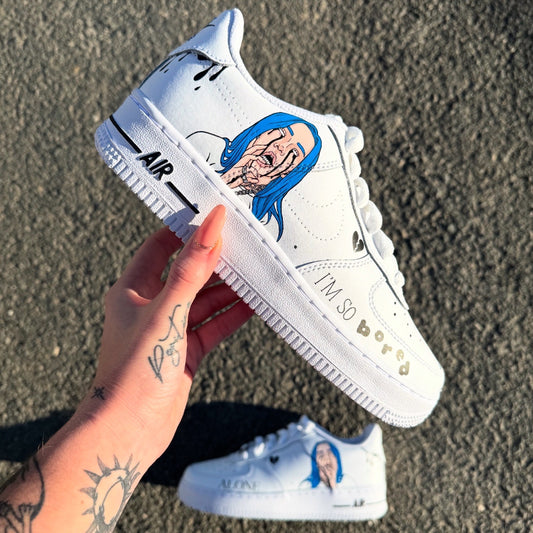 Nike Air Force 1 personalizadas de Billie Eilish con retratos pintados a mano en azul en los laterales externos y las inscripciones "I’m so bored" y "Alone" en la parte delantera de los zapatos.
