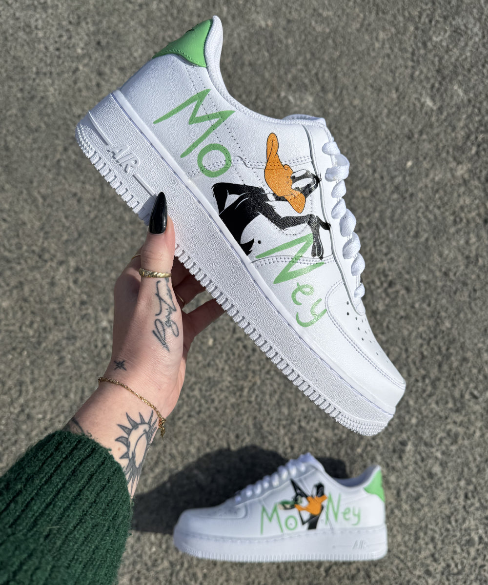 Nike Air Force 1 Custom Daffy Duck Money : dessins peints à la main du célèbre personnage et lettrage "Money" pour un style cartoon unique.