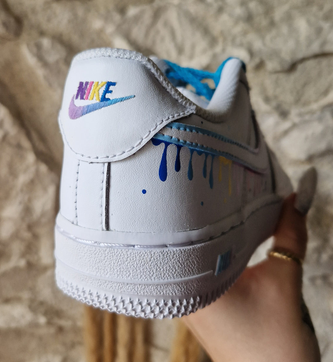 Zapatilla izquierda de Nike Air Force 1 personalizada a mano con detalles de gotas multicolor pastel en el swoosh.