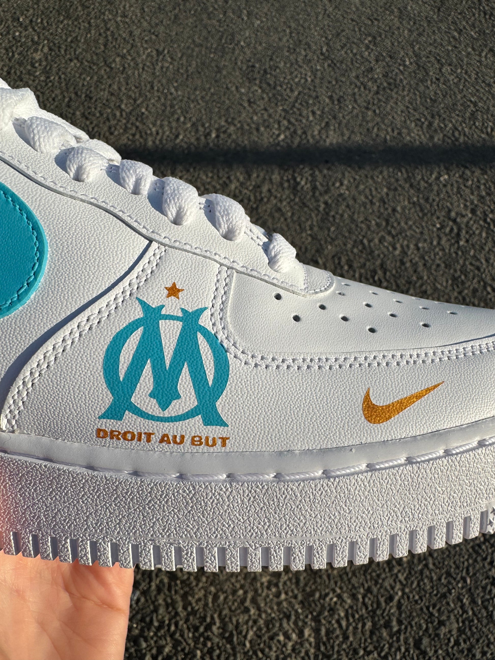 Vue sur l'avant externe de la chaussure, avec le logo de l'Olympique de Marseille et le logo Nike.