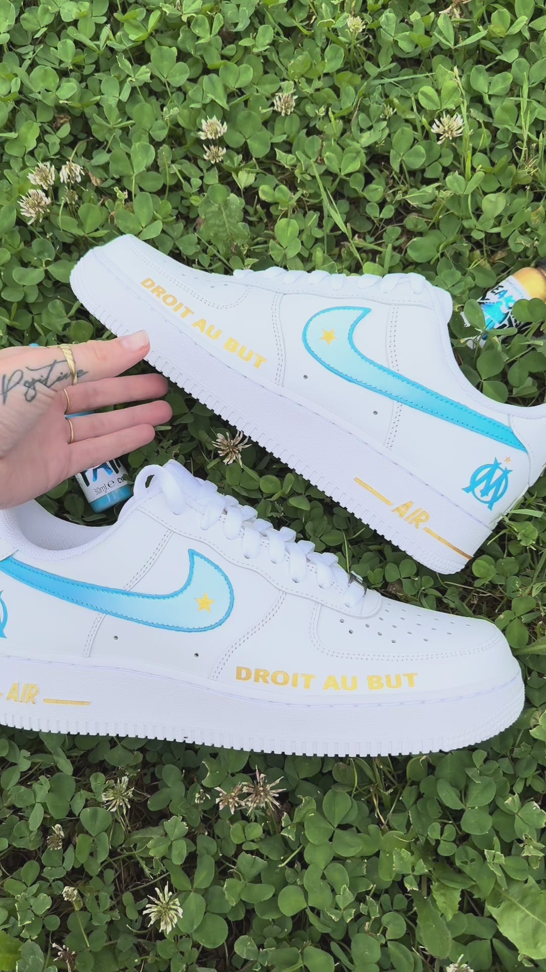 Modèle présenté : Nike Air Force 1 Custom OM – Droit au but. Swoosh dégradés bleu et blanc, étoile dorée, logo OM à l’arrière et inscription “DROIT AU BUT” en doré sur l’avant. Peinture à la main, finition résistante à l’eau, pour une paire unique et fidèle à l’esprit du club.